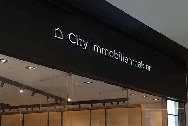 Schwarzes Ladenschild 'City Immobilienmakler' über beleuchtetem Schaufenster